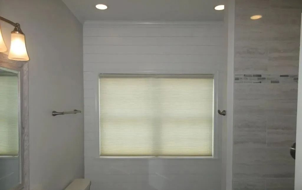 Bathroom interior with frosted window, wall sconces, and light gray tile shower surround