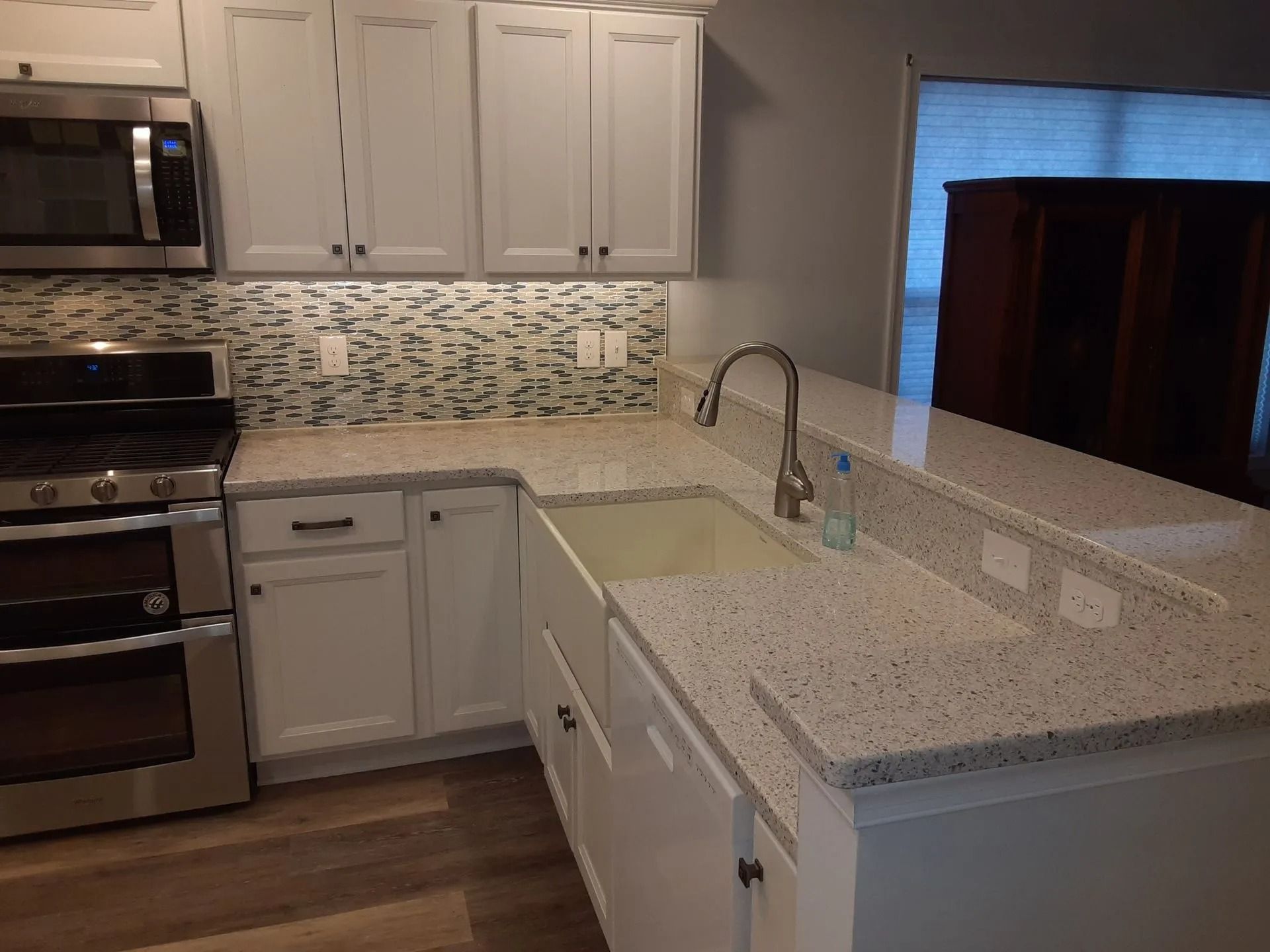 Modern kitchen with white cabinets, stainless stove, speckled counters, and mosaic tile backsplash