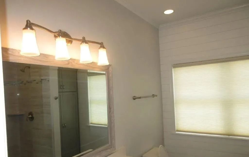 Bathroom with lit vanity mirror, double sink, towel rack, and frosted window blinds