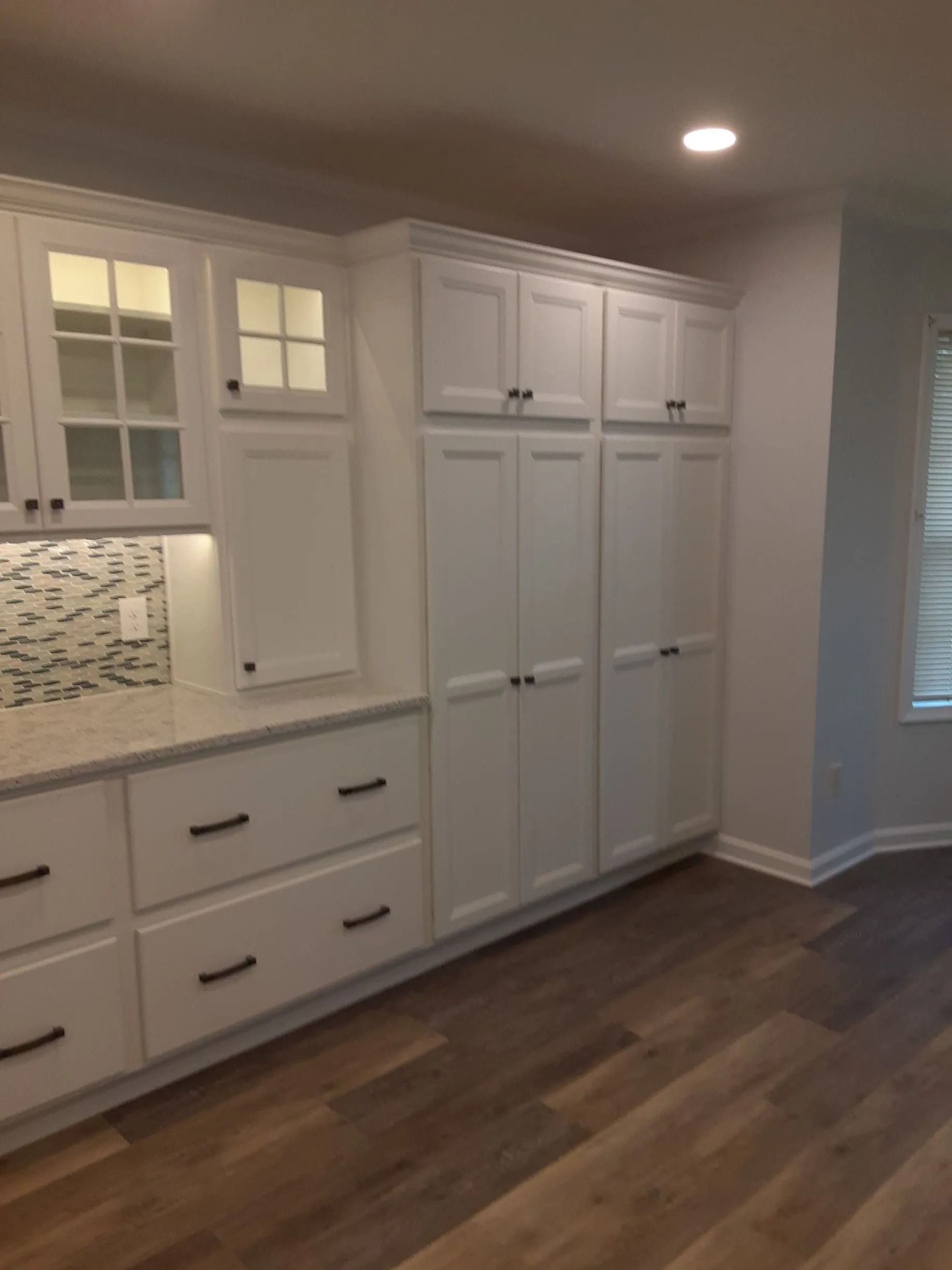 Built-in white cabinets and drawers along a wall in a modern room with wood floors and recessed lighting