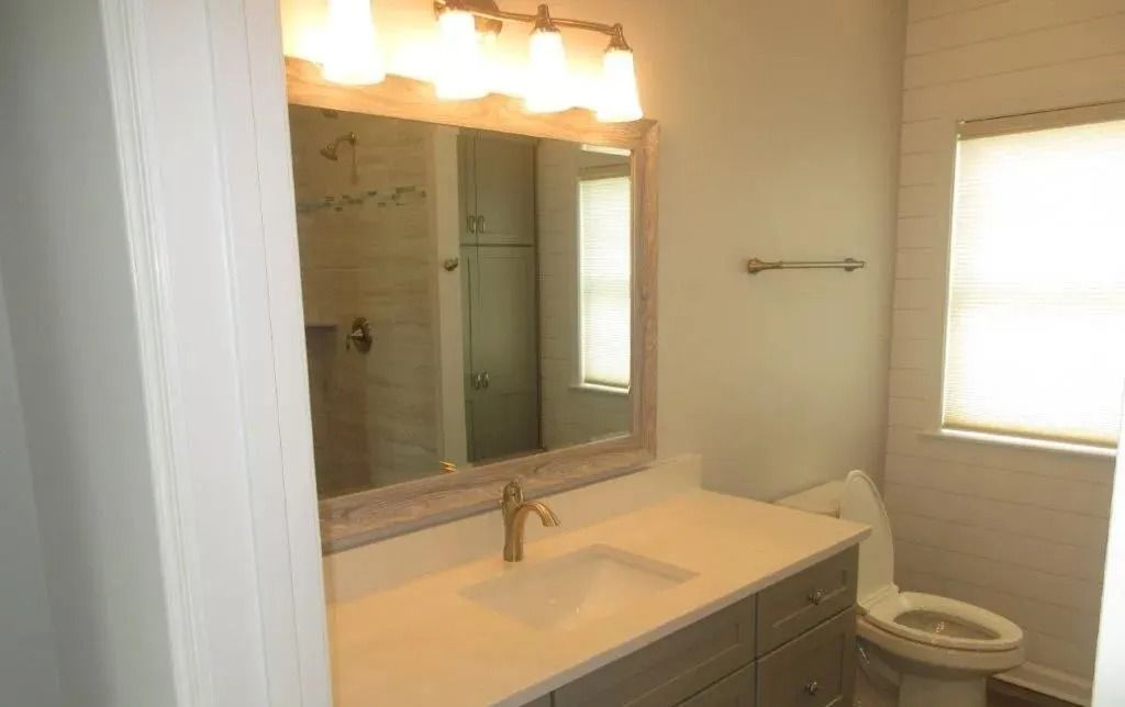Bright bathroom with vanity, large mirror, and toilet by a window