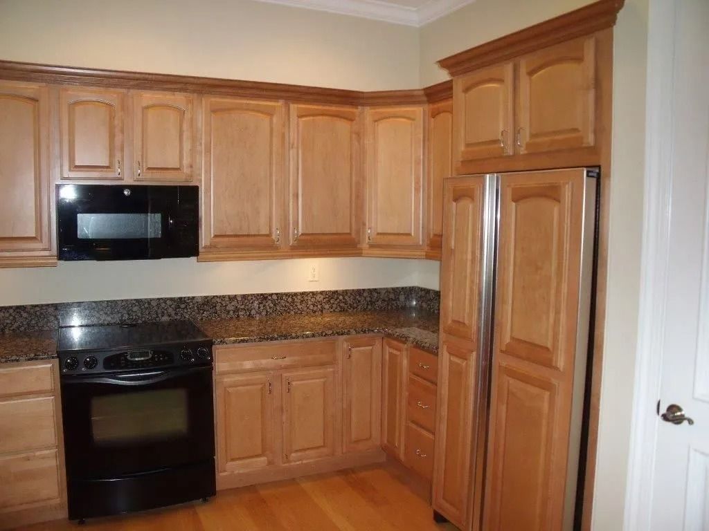 Wooden kitchen with black appliances, granite countertop, and tan walls