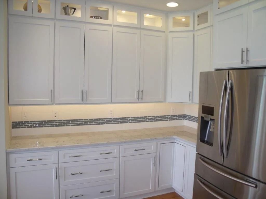 Bright white kitchen with upper and lower cabinets, marble backsplash, and stainless steel refrigerator