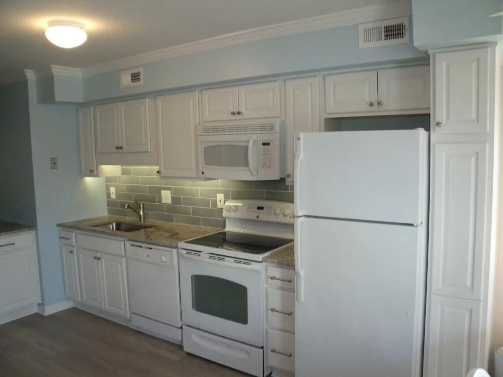 White kitchen with white cabinets, stove, microwave, refrigerator, and gray backsplash.