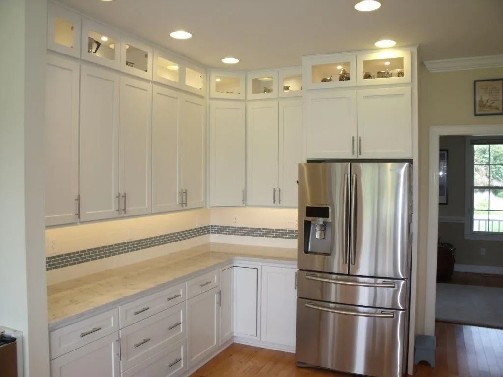Bright white kitchen with light wood countertops, white cabinets, and a stainless steel refrigerator.