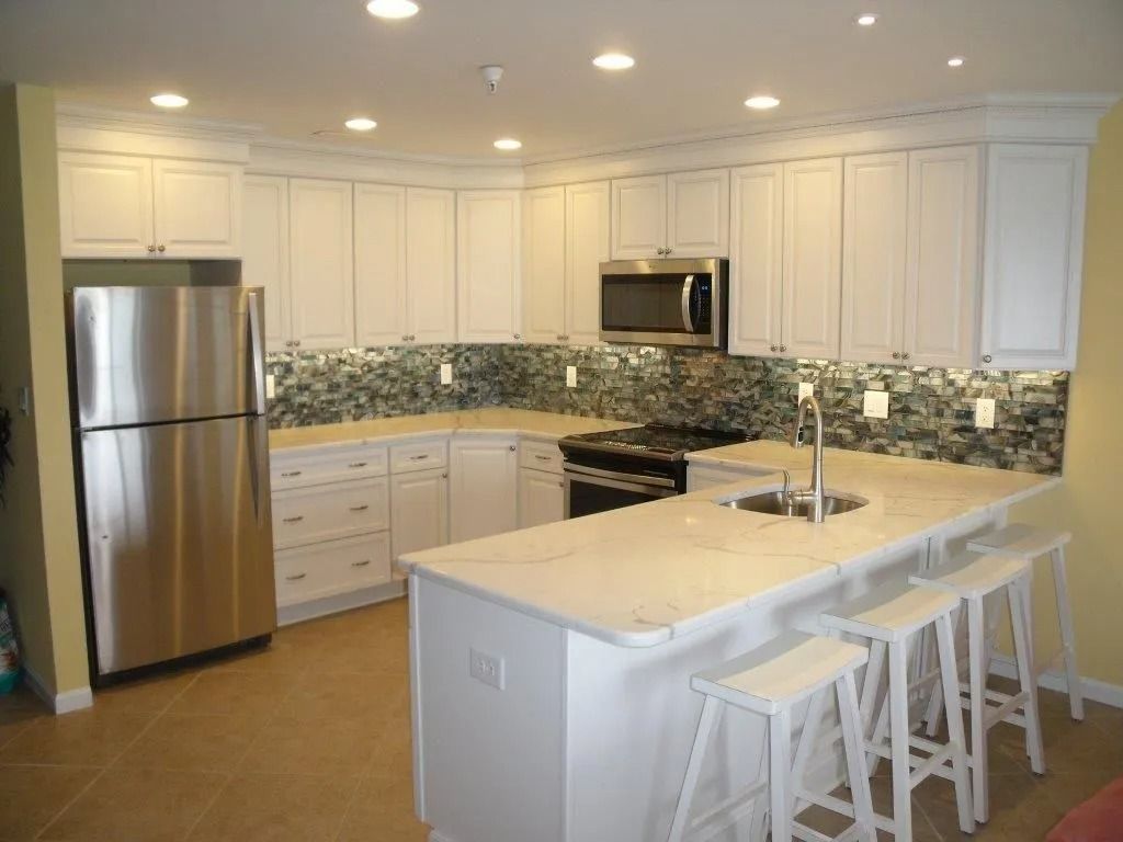 Bright modern kitchen with white cabinets, stainless steel appliances, mosaic backsplash, and a central island with stools