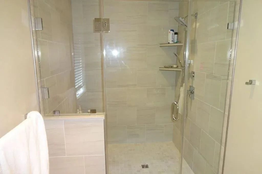Small beige-tiled bathroom with a glass shower, towel rack, and shelves.
