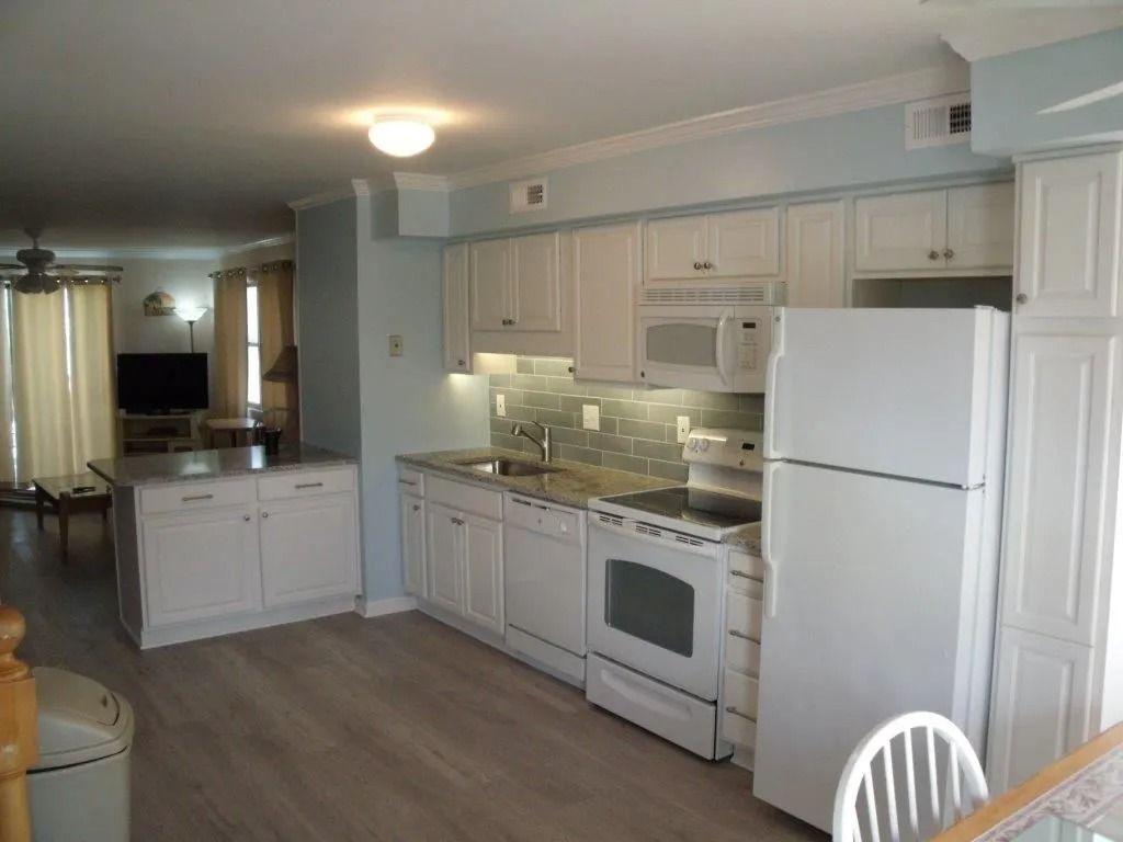 Bright white kitchen with refrigerator, stove, cabinets, and light wood flooring; open layout to dining area