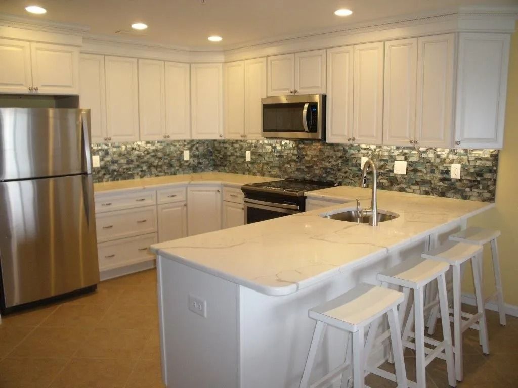 Bright modern kitchen with white cabinets, stainless appliances, island, and four white stools