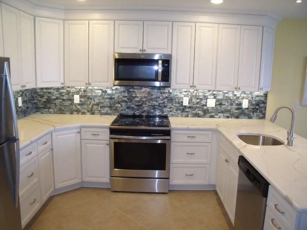 Modern kitchen with white cabinets, stainless steel appliances, mosaic backsplash, and light countertops