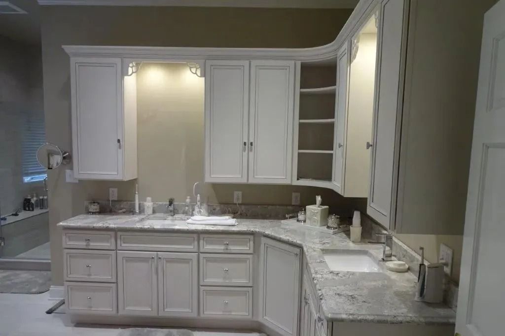 White kitchen with cabinets, granite countertops, and a central sink under warm under-cabinet lighting