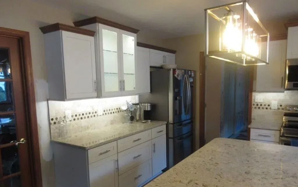 Modern kitchen with white cabinets, granite island, stainless fridge, and pendant lights