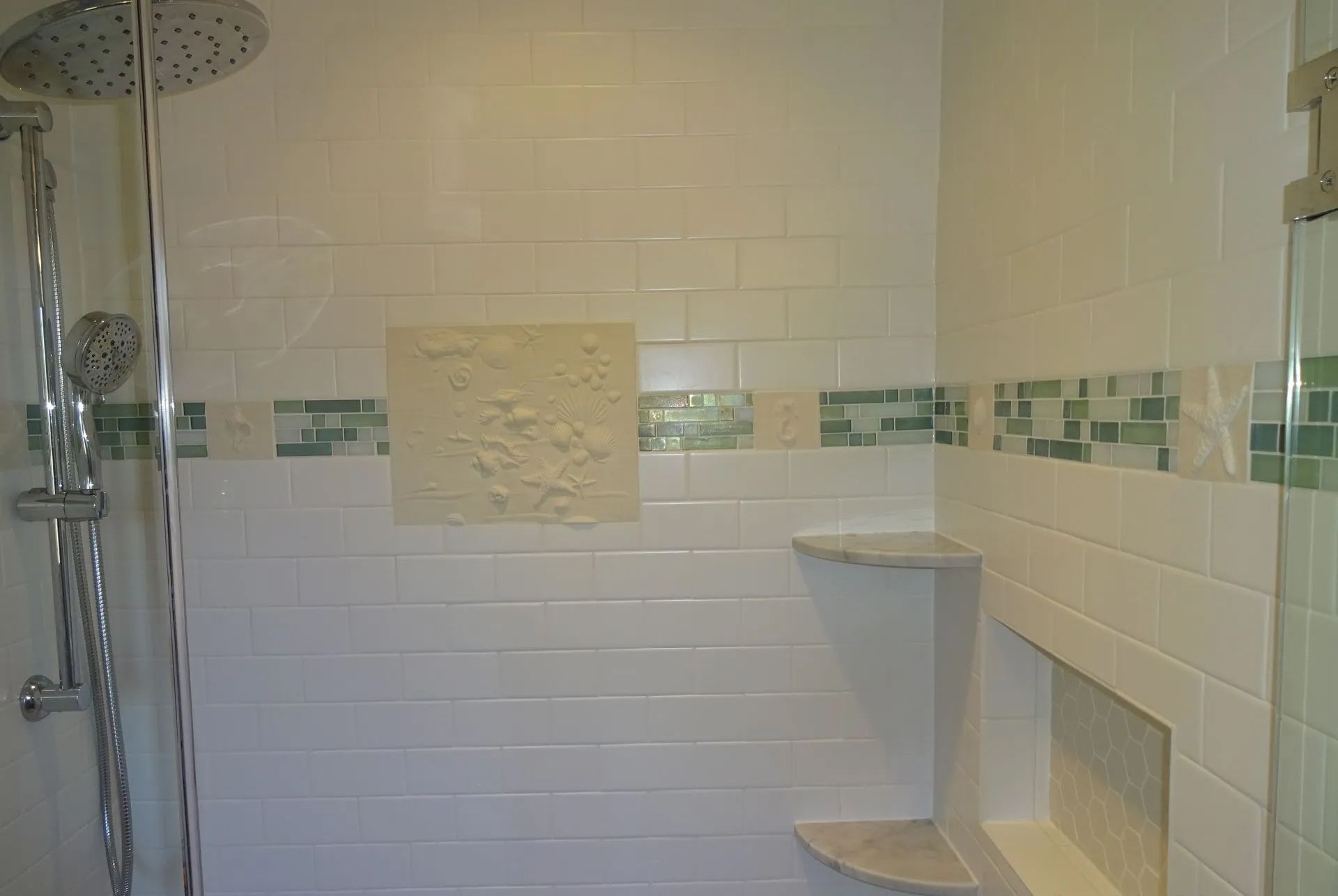 White tiled bathroom shower with green accent border, showerhead, corner shelf, and built-in soap niche