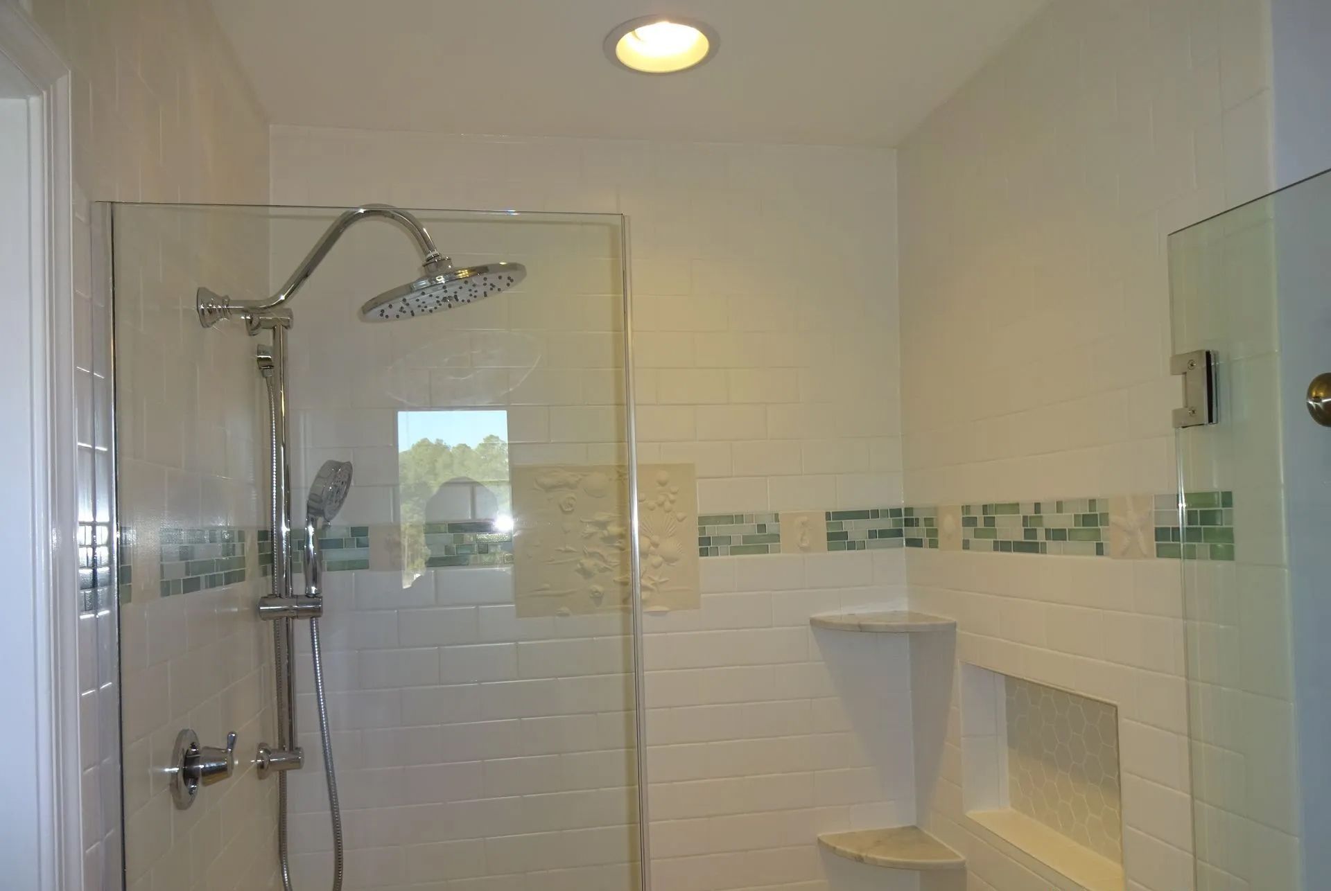 Modern white-tiled walk-in shower with glass door, chrome fixtures, and a built-in shelf.