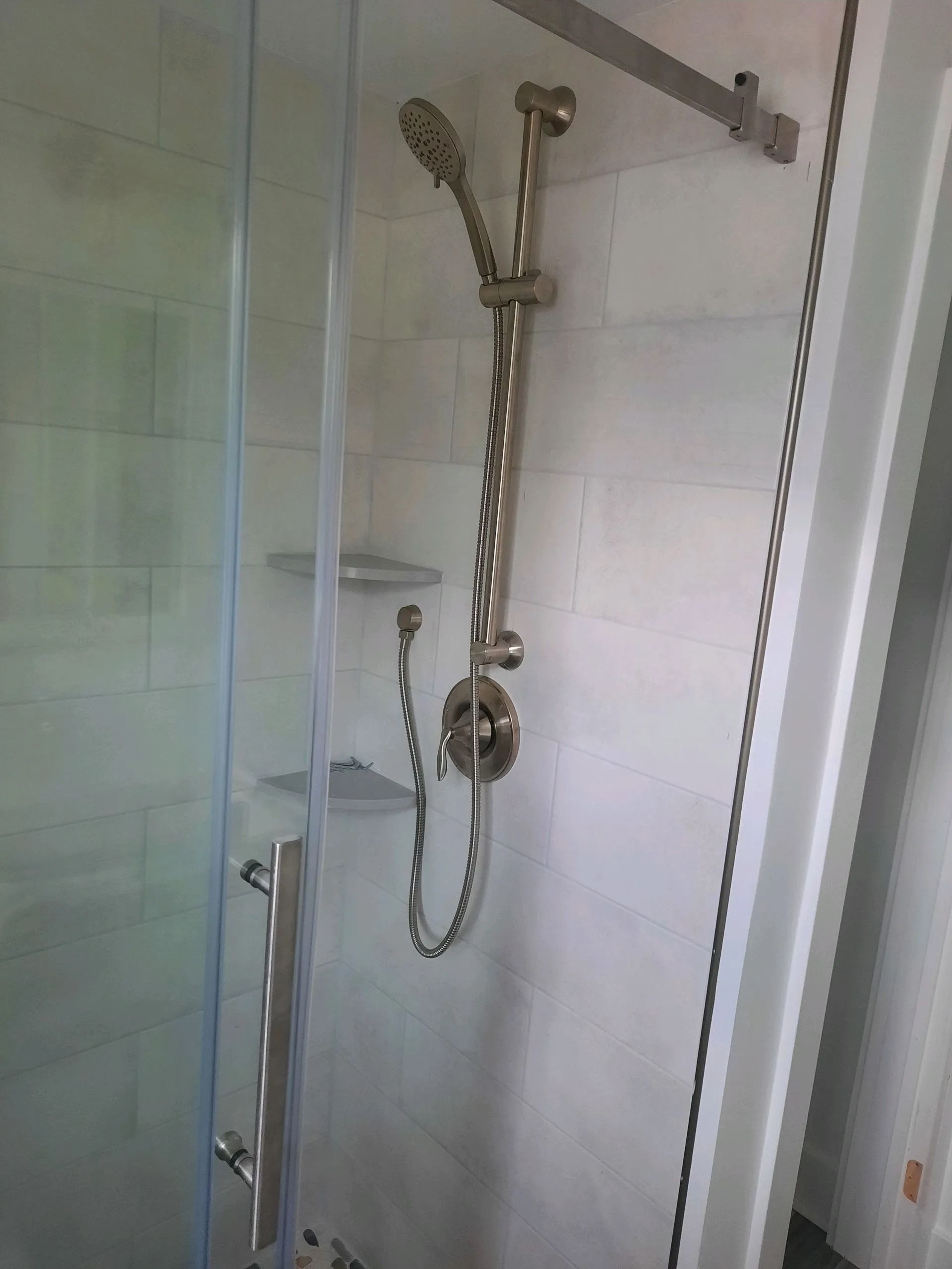 Glass shower stall with handheld showerhead, wall-mounted grab bar, and built-in shelf.