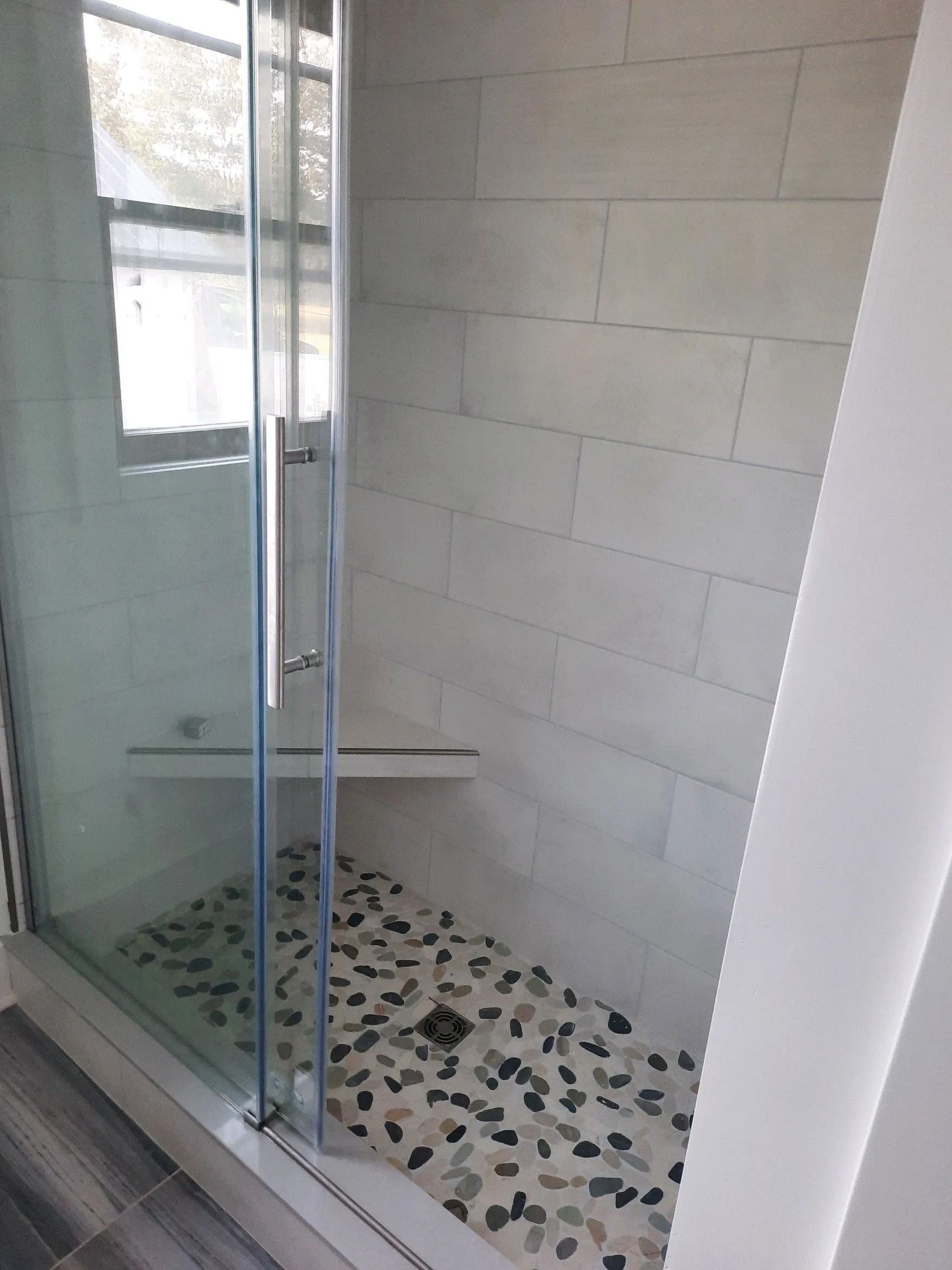 Glass-enclosed shower with white tile walls and pebble floor in a bathroom