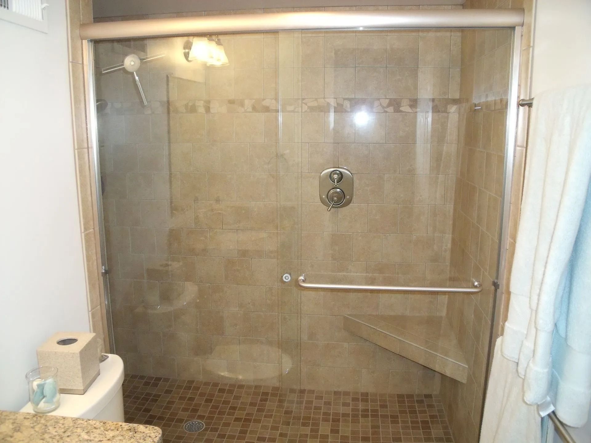 Tiled walk-in shower with glass door and chrome grab bar in a bathroom.