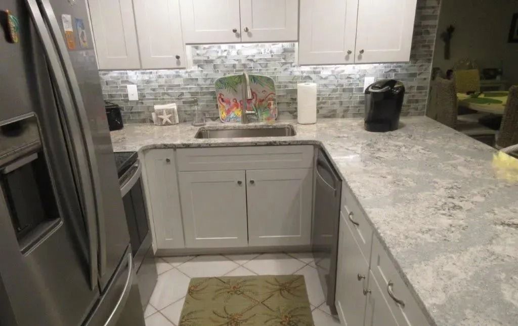 Bright kitchen with white cabinets, gray countertops, stainless fridge, and a coffee maker on the counter