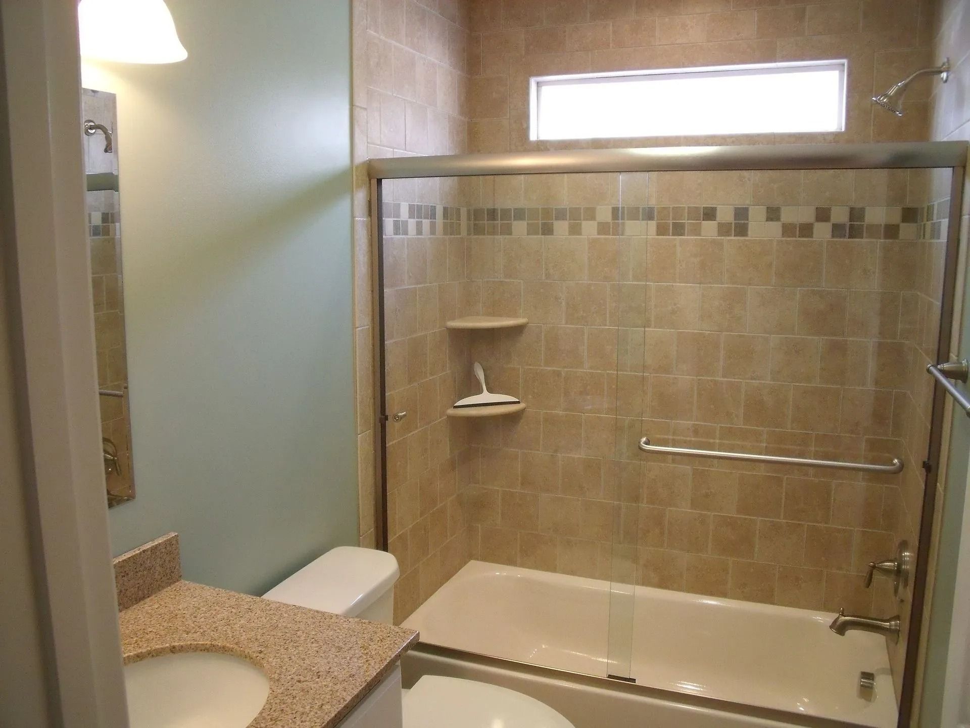 Bathroom with a glass-enclosed bathtub, beige tile walls, and a granite counter next to a toilet.
