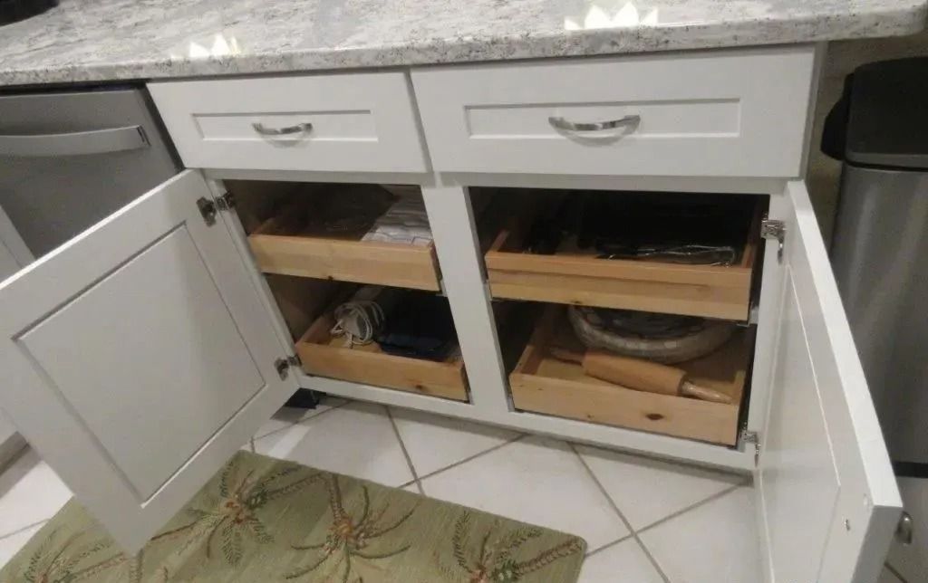 Open cabinet under a countertop with pull-out drawers and storage bins inside.