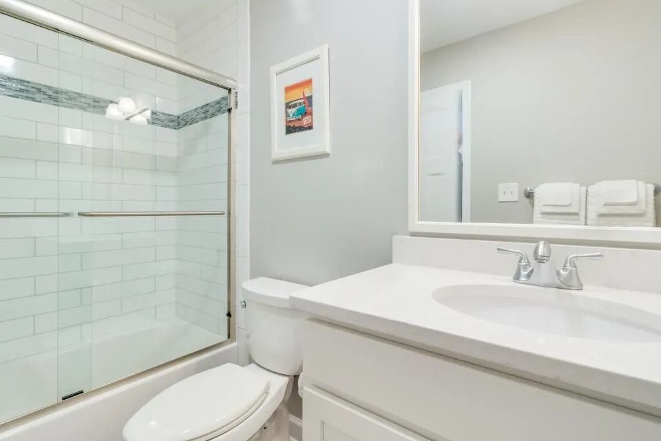 Bright white bathroom with glass shower, toilet, and vanity sink with mirror