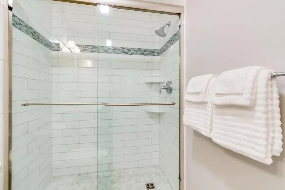 Glass shower with white tile and a towel rack holding folded white towels