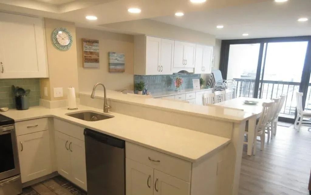 Bright modern kitchen with island, white cabinets, and dining table by large window.
