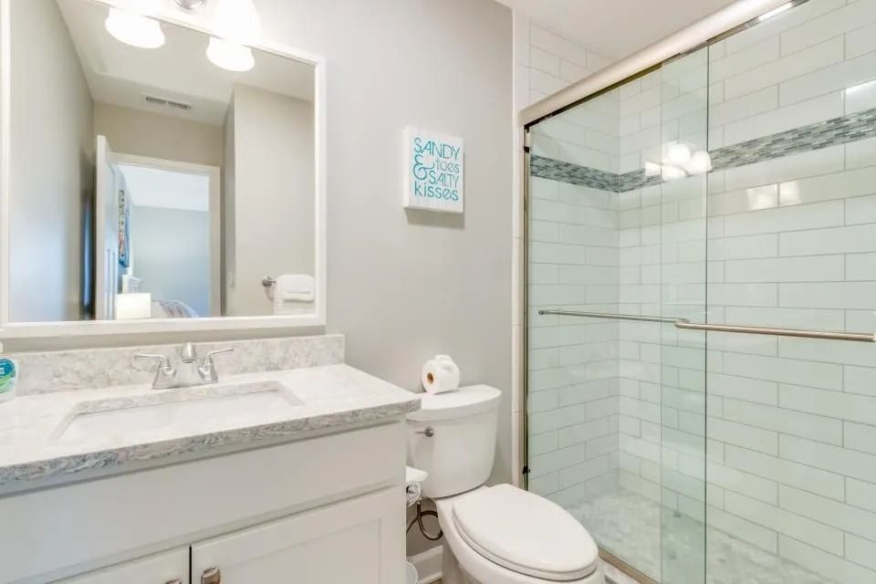 Bright modern bathroom with white vanity, mirror, toilet, and glass-enclosed shower with white tile.