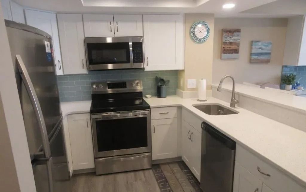 Modern white kitchen with stainless steel appliances, island sink, and light blue backsplash