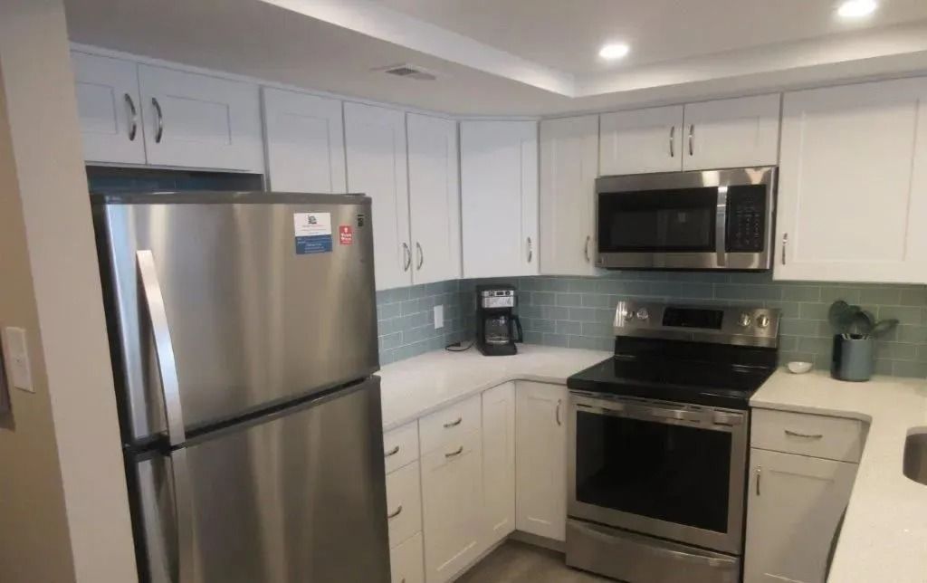 Modern kitchen with stainless steel appliances, white cabinets, and light blue backsplash tiles.