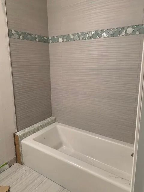 Corner bathtub in a tiled bathroom with gray walls and a decorative border