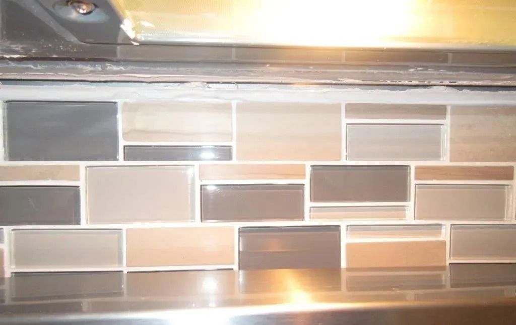 Rectangular beige, gray, and brown mosaic tile backsplash with bright glare from overhead light