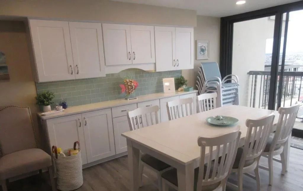 Bright kitchen and dining area with white cabinets, table, chairs, and sliding glass door to balcony