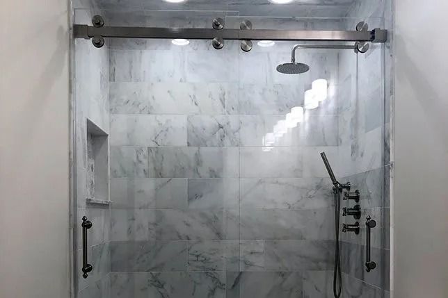 Bathroom shower with marble-tile walls, glass enclosure, and metal fixtures