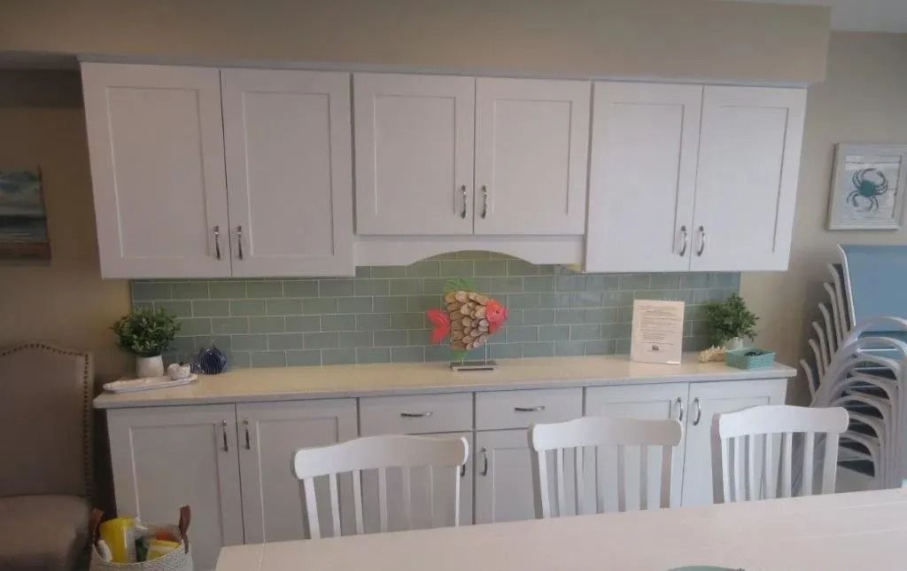 Bright kitchen with white cabinets, pale blue backsplash, and a white island with chairs and flowers.