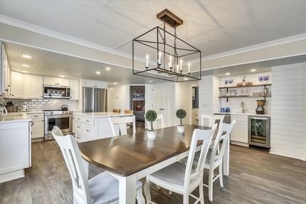 Bright white kitchen and dining area with a long wooden table and white chairs under a modern chandelier