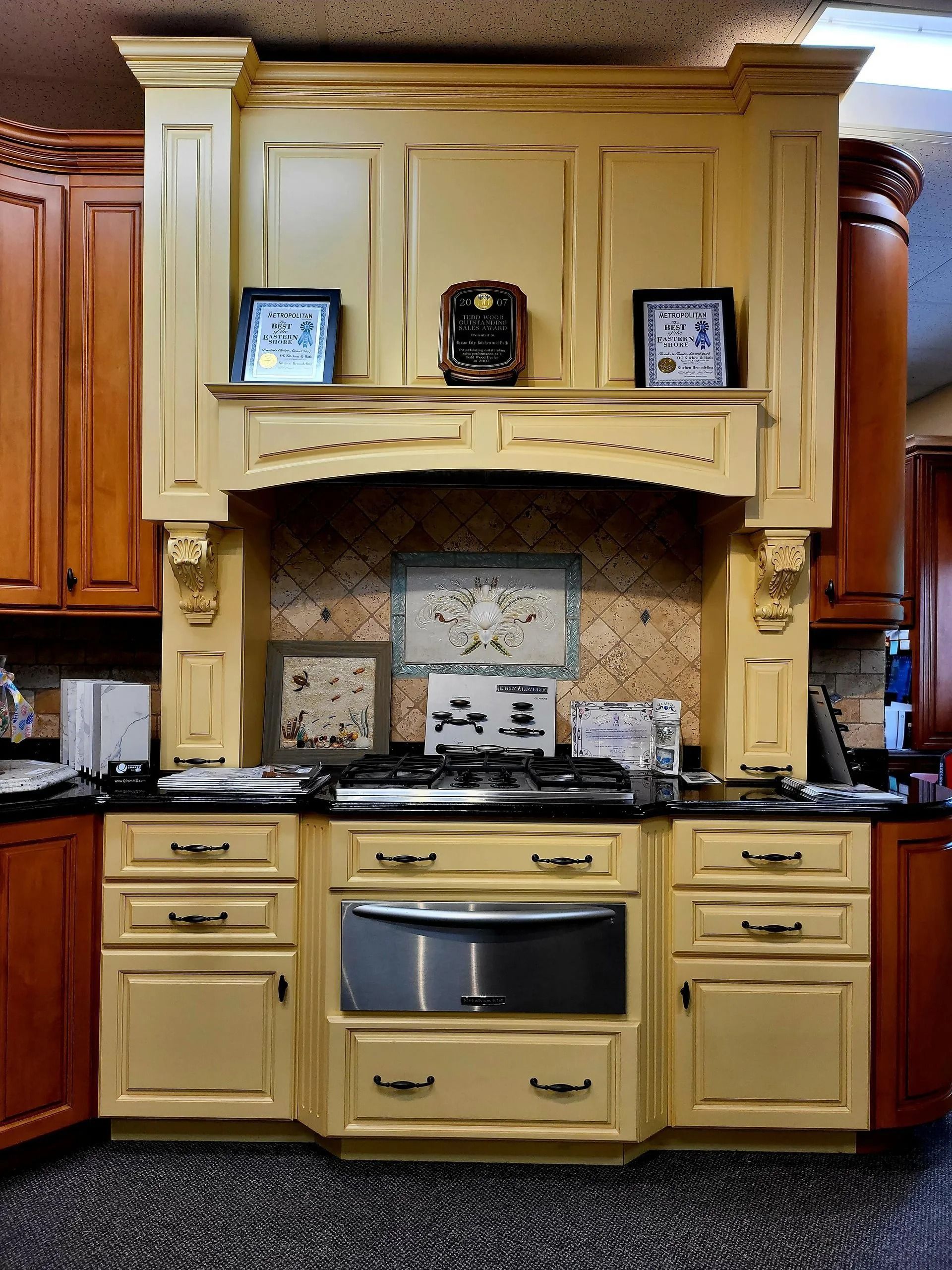 Cream kitchen with built-in wall oven, black countertop, and decorative display shelves above the stove.