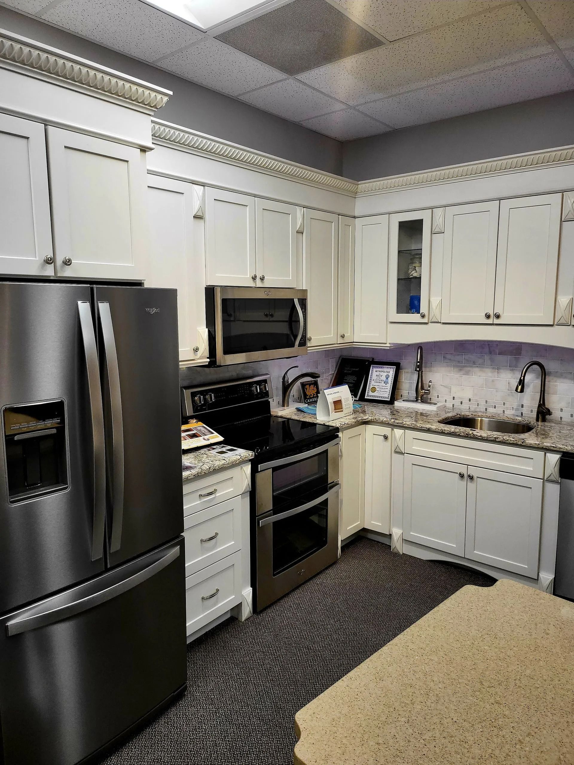 Bright kitchen with black stainless appliances, white cabinets, tiled backsplash, and beige rug