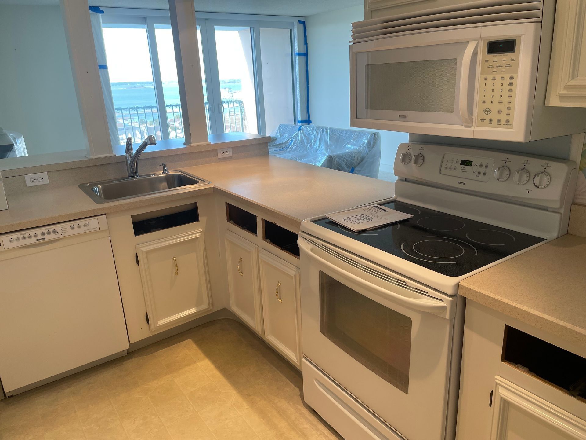 Bright kitchen with white cabinets, stove, microwave, sink, and a large window overlooking water.