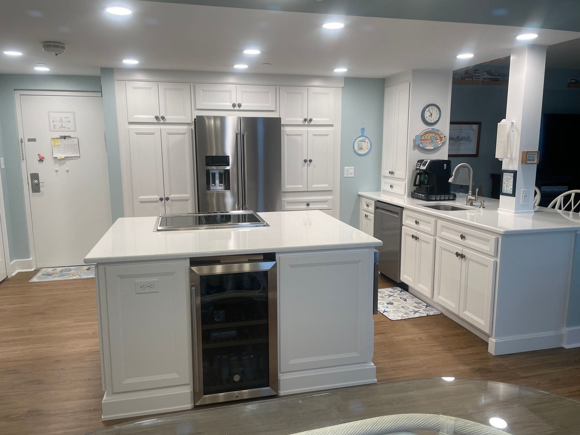 Bright white kitchen with island, stainless steel refrigerator, and hardwood floors.
