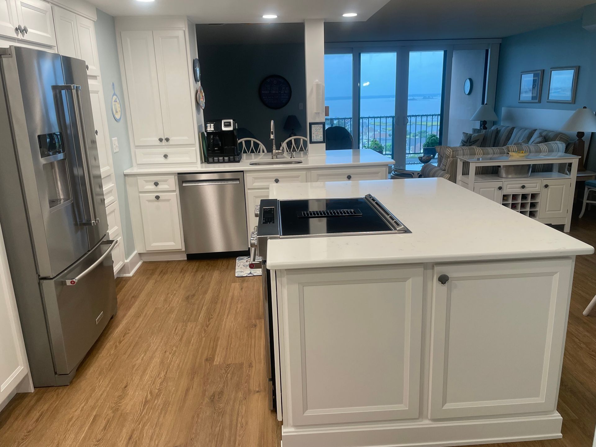 Bright white kitchen with stainless steel appliances, island, and large windows overlooking water.