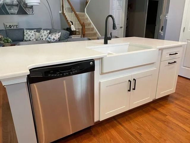 Modern kitchen with white island, stainless dishwasher, deep sink, and black faucet on wood floor