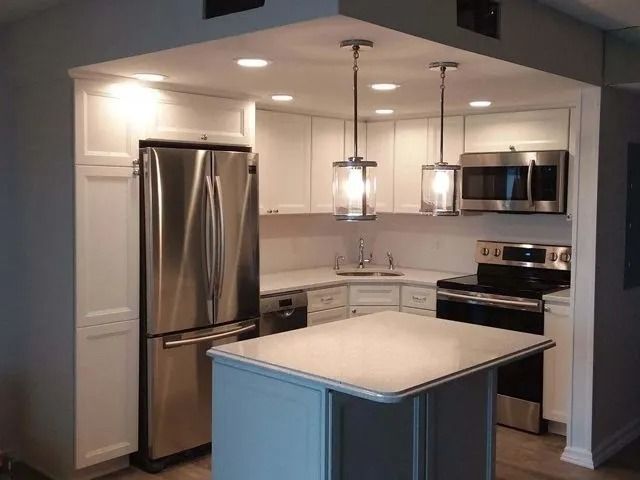 Modern kitchen with stainless steel appliances, white cabinets, and a blue island under pendant lights