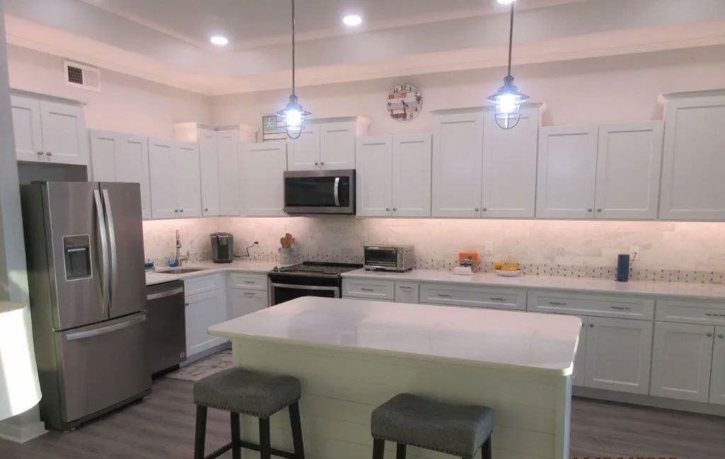 Modern white kitchen with stainless steel appliances, island, and two dark stools