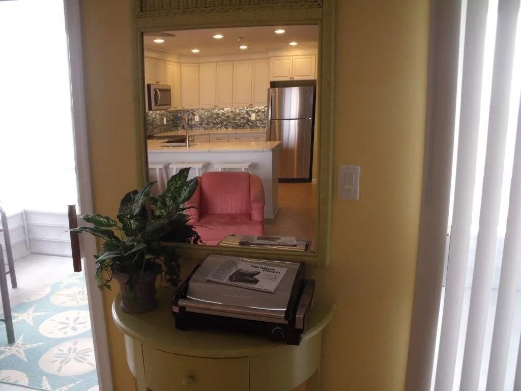 Living room view into kitchen, with pink chair, potted plant, and a typewriter on a table