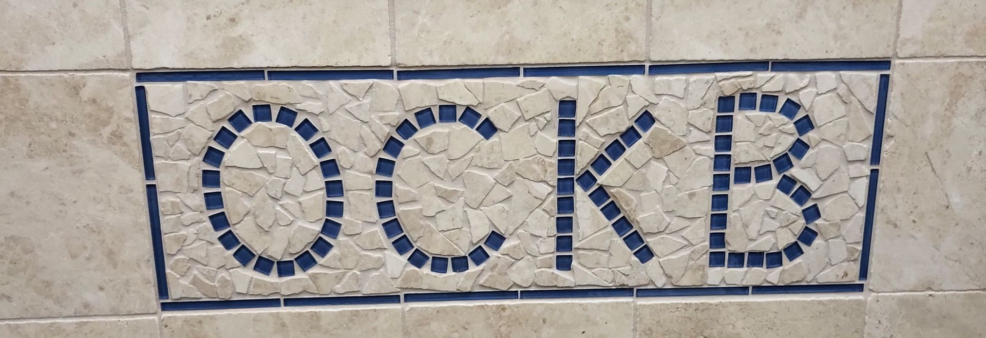 Blue tiled letters “OCKB” on a beige stone wall panel