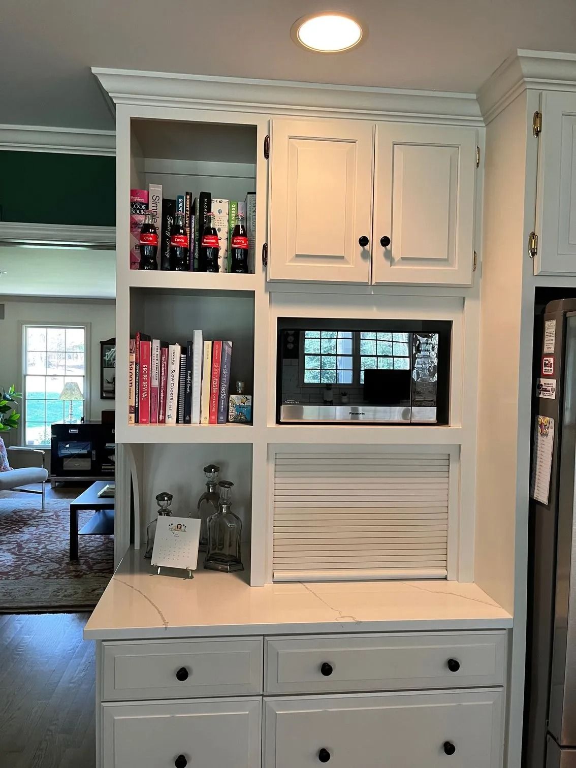 Built-in kitchen hutch with shelves, white cabinets, drawers, books, bottles, and a microwave niche