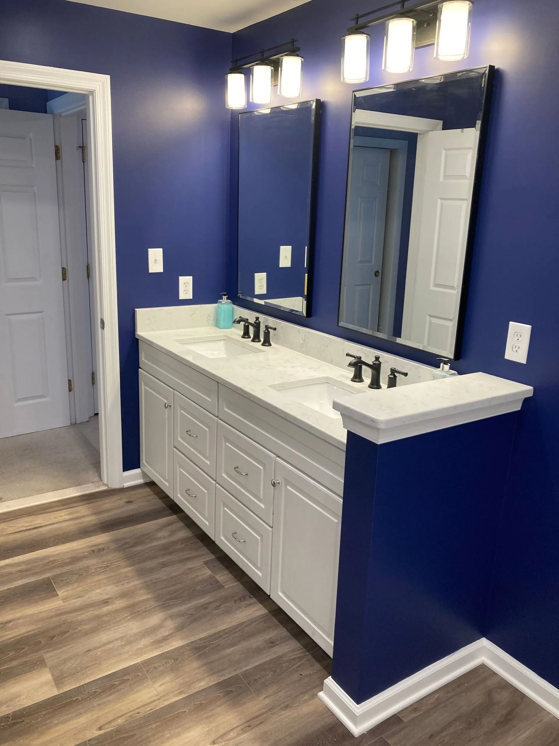 Blue bathroom with white vanity, mirror, and wall lights, seen from the doorway.