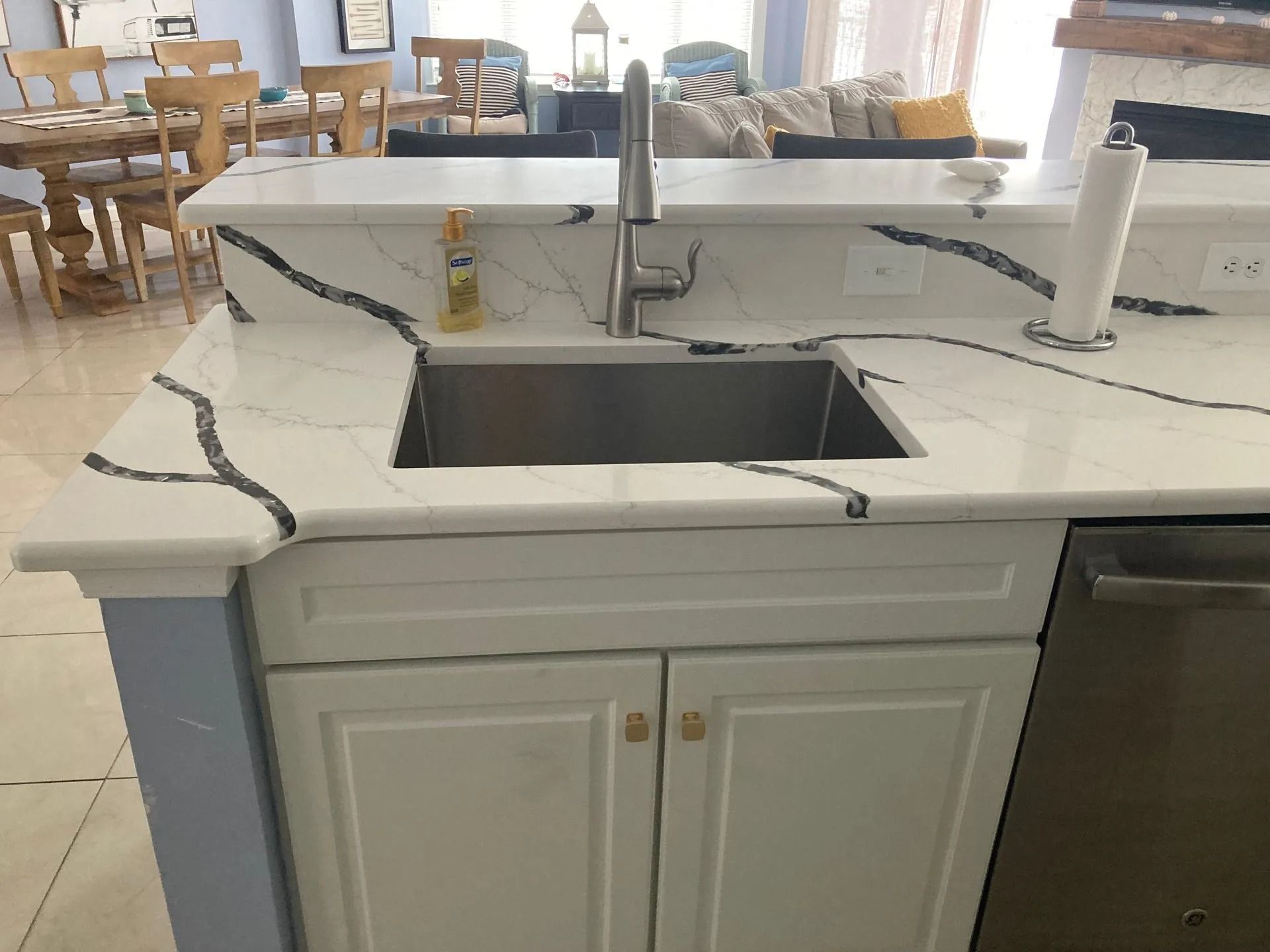 White kitchen sink island with open rectangular basin, countertop outlets, and dining chairs in the background