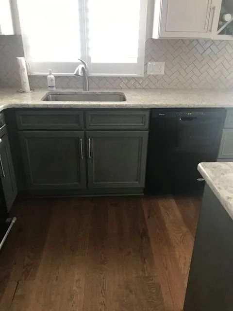 Kitchen with dark cabinets, stainless sink under a window, and wood floors.